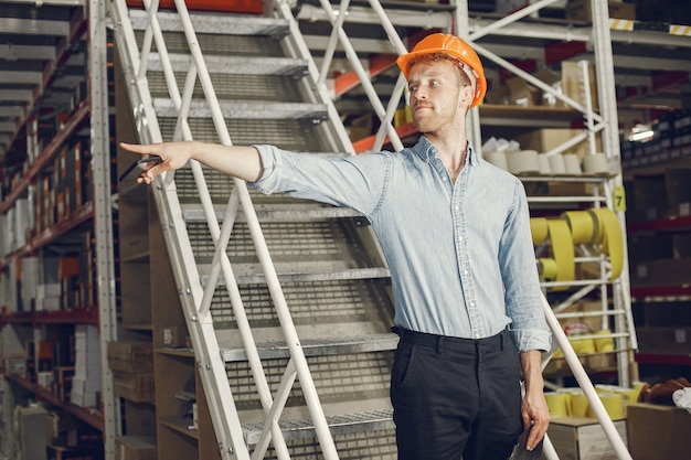 Industrial worker indoors in factory. Businessman with orange hard hat. Man in a blue shirt.