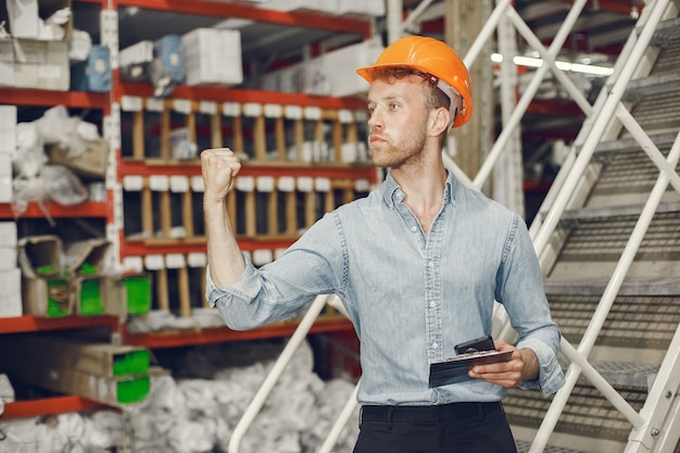 Industrial worker indoors in factory. Businessman with orange hard hat. Man in a blue shirt.