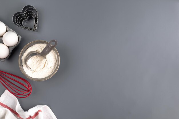 Ingredients for baking on a dark gray background: flour, eggs, butter, heart shape, whisk, textiles. top view. Copy space. Layout of a pie or cake recipe with cookies