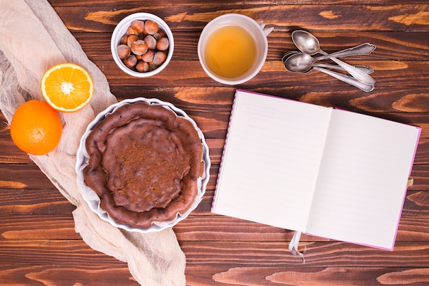 Ingredients for chocolate cake with spoons and white diary over the wooden desk