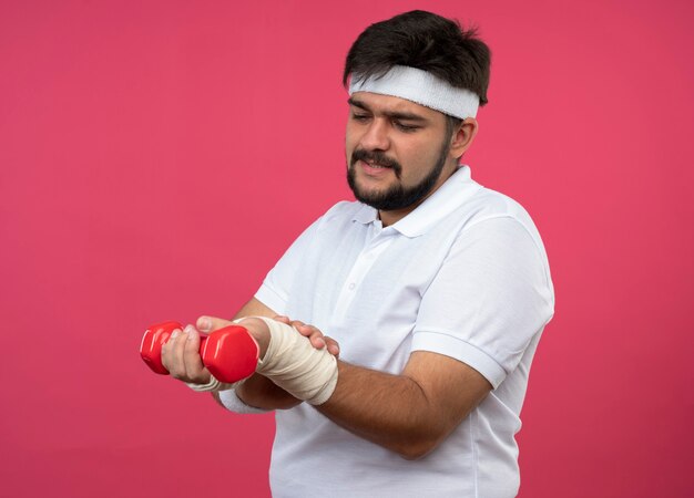 Injured young sporty man wearing headband and wristband with wrist wrapped with bandage