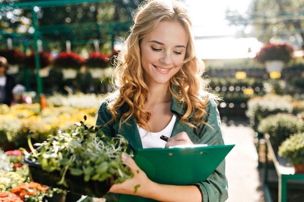 Inspector in botanical garden examines plants by writing data about them in notebook Lady poses with greenery among colorful flowers