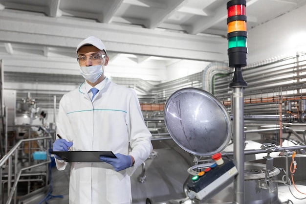 Free photo inspector in a mask and a scrub stands with a foldertablet in his hands at the dairy plant