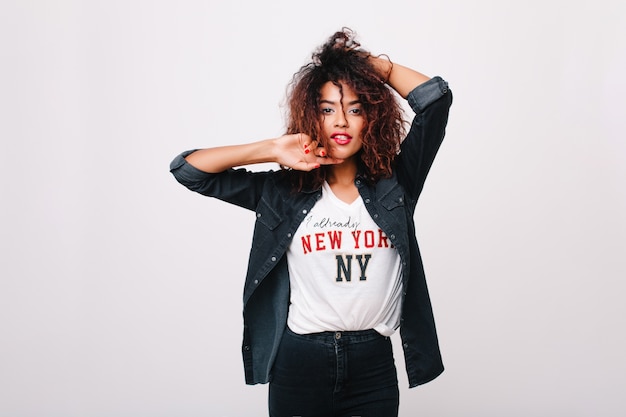 Free photo inspired african girl with shiny dark eyes posing with hands up. indoor portrait of fashionable black young woman with pretty face wears denim jacket.