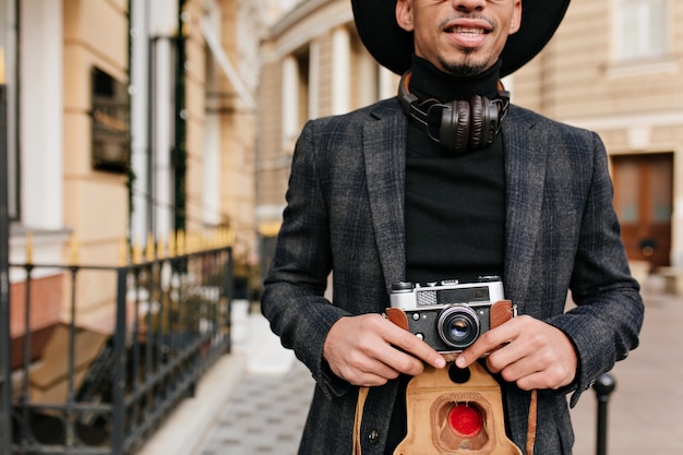 Free photo inspired african man wears black shirt standing on street with camera in hands. outdoor shot of well-dressed photographer.