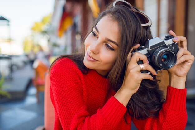 Inspired brunette woman having fun and making photos on her vacations . Cold season. Wearing stylish red knitted sweater.