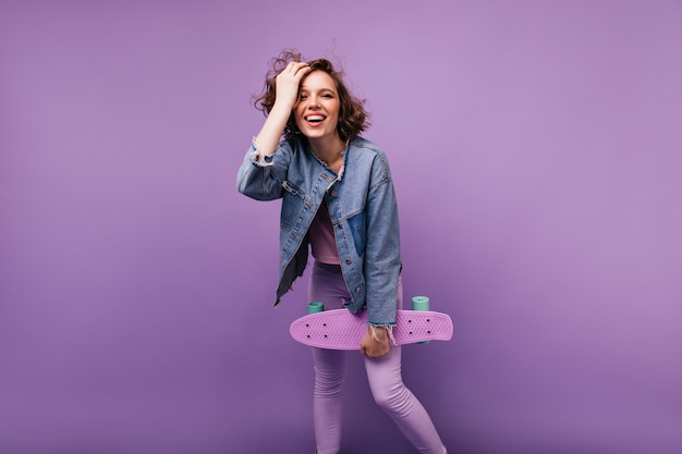 Inspired caucasian woman in casual attire expressing good emotions. Carefree curly girl with skateboard standing.