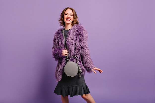 Inspired female model with cute gray purse looking to camera with smile