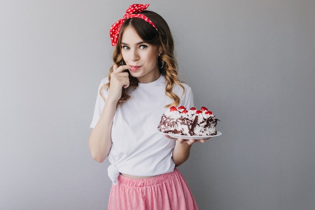 Inspired girl with wavy hair tasting birthday cake. enchanting female model with pie posing.