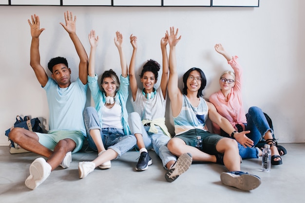 Inspired students happy posing with hands up because exams is over. Indoor portrait of blissful university mates having fun in campus before holidays..