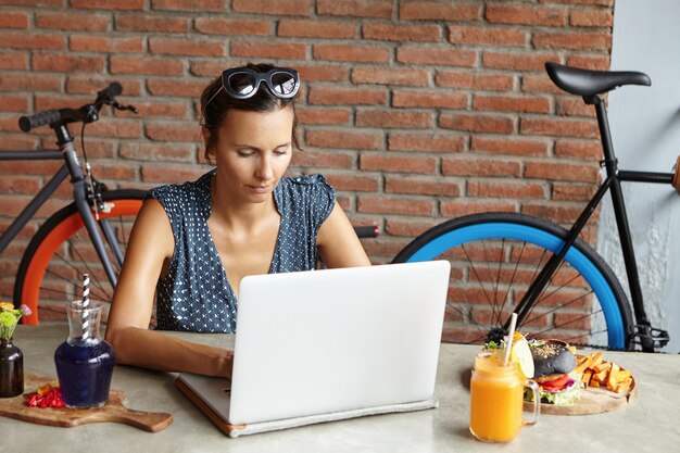 Inspired woman blogger working on new post for her blog, reading comments of her followers and smiling. Female with shades on her head enjoying online communication