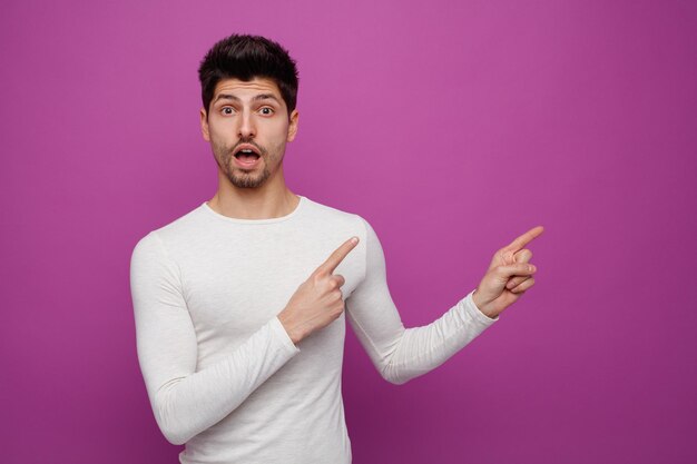 Inspired young handsome man looking at camera pointing to side on purple background