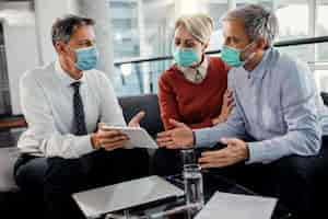 Free photo insurance agent and couple wearing face masks while using touchpad in the office