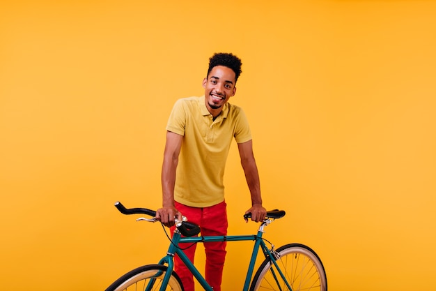 Free photo interested african male model in red pants smiling. portrait of inspired black guy standing near green bicycle.