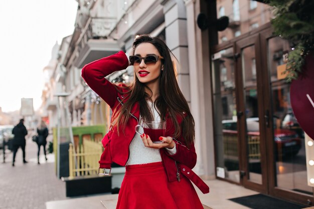 Interested caucasian lady in black glasses posing with cup of tea