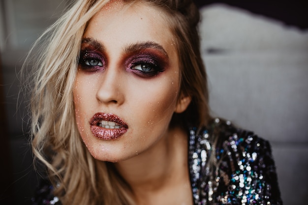 Interested white girl with glitter makeup. Indoor shot of enthusiastic caucasian woman with trendy hairstyle.