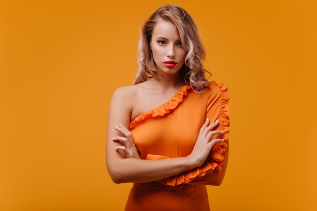 Free photo interested woman in stylish orange dress posing with arms crossed