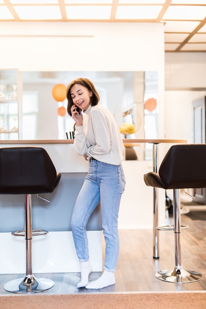 Free photo interested woman with phone standing in panoramic kitchen in casual clothes