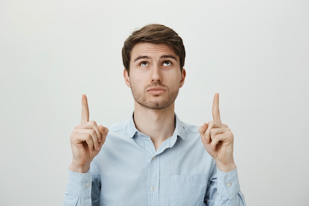 Free Photo intrigued bearded young man looking and pointing up at advertisement