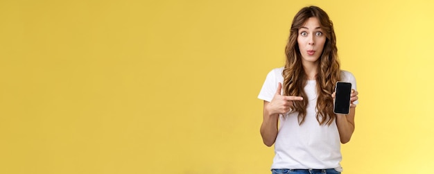 Free photo intriguing app check out enthusiastic surprised attractive girlfriend gossiping friend new boyfriend showing curious photo smartphone hold mobile phone pointing telephone screen yellow background