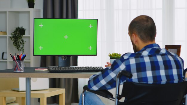 Invalid businessman waving during a video call on computer with green screen.