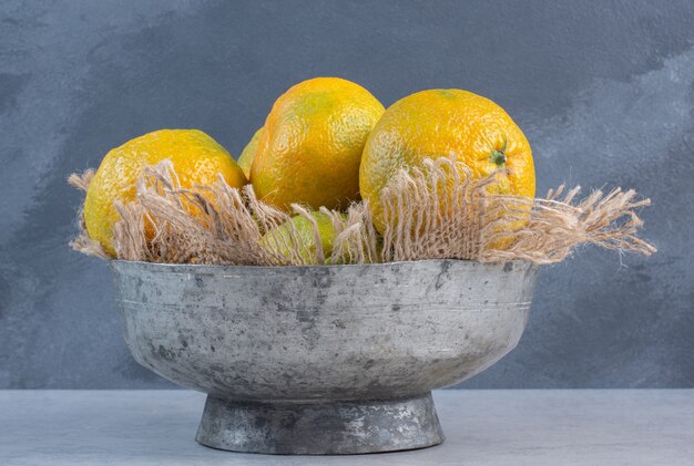 Iron bowl full of tangerine on grey background. 