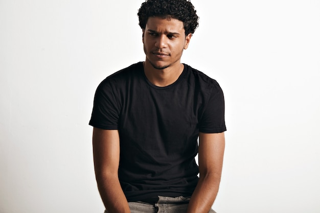 Ironic thoughtful handsome young man with an afro wearing a black sleeveless cotton t-shirt on white wall