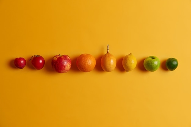 Free Photo isolated citrus fruit in row against yellow background. green lime, apple, lemon, cumquat, orange, fortunella and peach. nutritious tropical fruits offering host of vitamins to keep you healthy