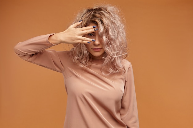 Free Photo isolated of cute mysterious young european woman with pinkish voluminous hair holding hand over her eye, peeping at you through fingers, having curious playful look