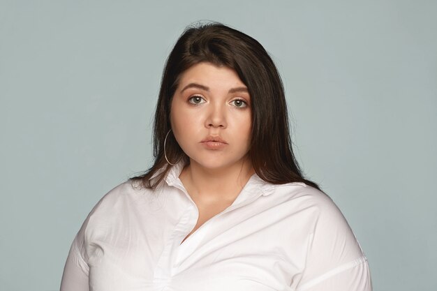 Isolated image of emotional expressive young dark haired chubby female wearing white formal shirt pouting lips having disappointed offended facial expression, doesnt want to work extra hours