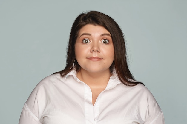 Isolated image of funny buy eyed plus size female manager in white formal shirt expressing astonishment, staring in full disbelief, shocked with unexpected news or gossip. Surprise and shock