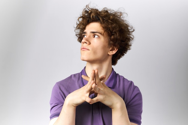 Free Photo isolated image of pensive young caucasian man with voluminous hairdo looking up clasping hands together, thinking or dreaming, making plans for future. body language and human facial expressions