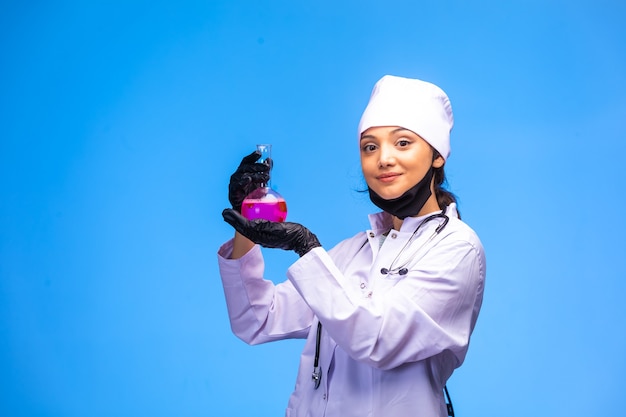 Isolated nurse in hand and face mask holds chemical flask and demonstrates it. 