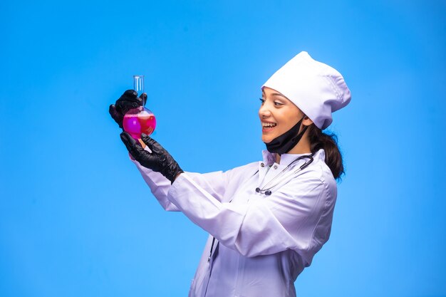 Isolated nurse in hand and face mask shows flask with pink liquid and smiles.