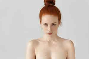 Free photo isolated portrait of attractive young caucasian female with ginger hair knot posing topless indoors