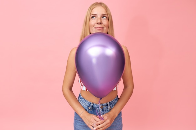 Free photo isolated portrait of fashionable joyful young european woman enjoying birthday party, holding shiny helium balloon