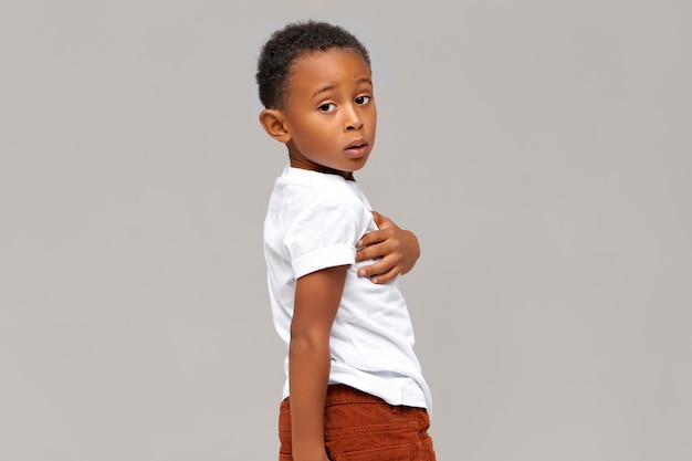 Free photo isolated portrait of perplexed dark-skinned boy dressed in white t-shirt .handsome african child posing . body language