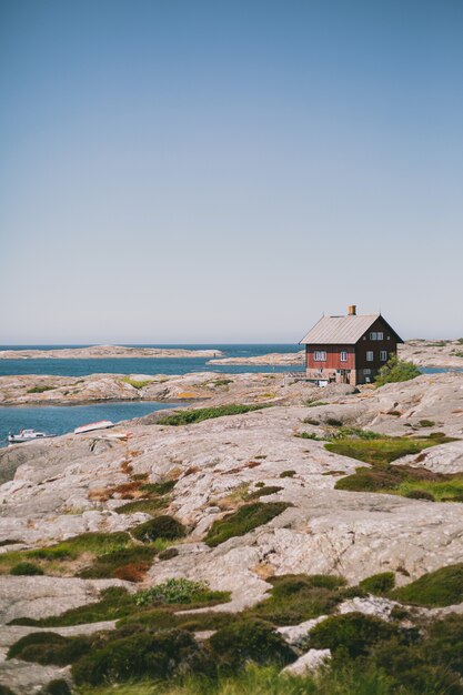 Isolated red wooden house on the shore near the ocean under the blue sky on a sunny day