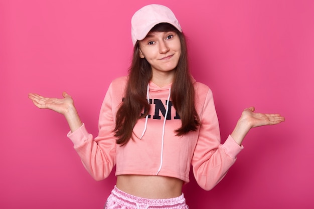 Isolated shot of attractive brunette pretty teenager, wears rose hoodie and cap