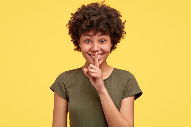 Isolated shot of cheerful young African American female makes silence sign