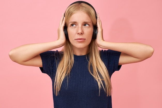 Free photo isolated shot of cute teenage girl holding hands on ears, enjoying high quality music tracks in mp3 player using wireless headset