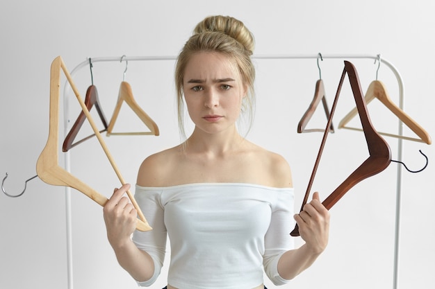 Free Photo isolated shot of frustrated upset young woman in white top holding empty racks doesn't know what to wear on date, having unhappy look. people, lifestyle, wardrobe, clothes and fashion concept