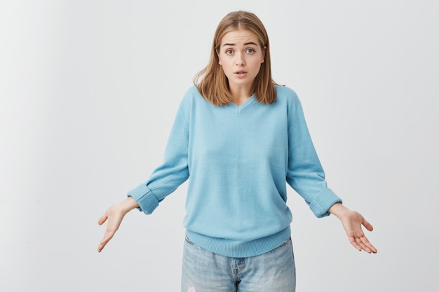 Free photo it's not a big deal. clueless cute girl dressed in blue sweater and jeans shrugging shoulders and staring  with confused look after she did something wrong but not feeling sorry or guilty.