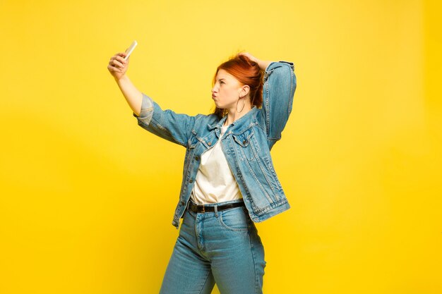 It's easier to be follower. Need minimum clothes for selfie. Caucasian woman's portrait on yellow background. Beautiful female red hair model. Concept of human emotions, facial expression, sales, ad.