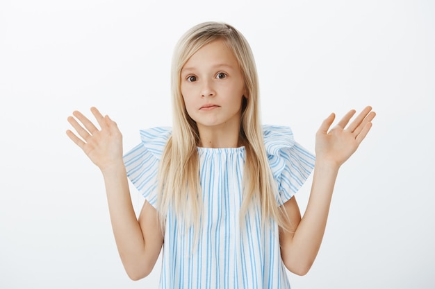 It was not me, I am innocent. Portrait of confused nervous little blond girl raising palms up in surrender and staring with clueless anxious expression, standing