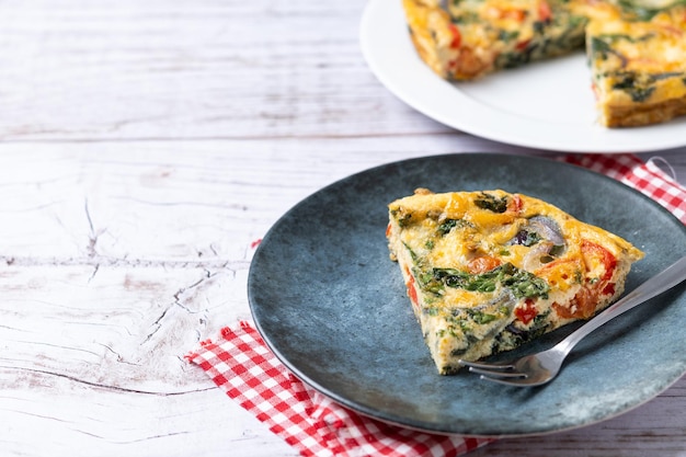 Italian Frittata made with spinach tomatoes onion and peppers on white wooden table