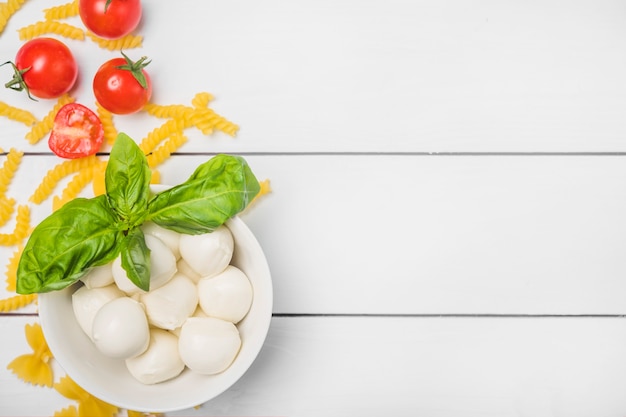 Free photo italian mozzarella cheese with basil leaf; tomatoes and fusilli pasta on white wooden plank