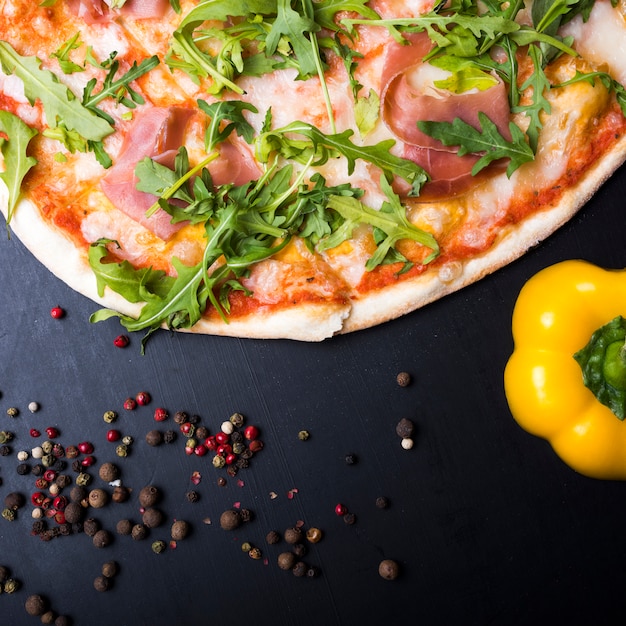 Free photo italian pizza; yellow bell pepper and black pepper on kitchen counter