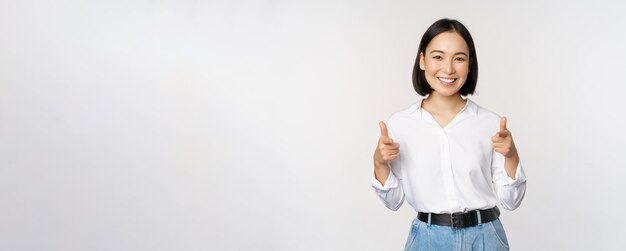 Its you congrats Smiling attractive asian woman businesswoman pointing fingers at camera with pleased face complimenting inviting you standing over white background