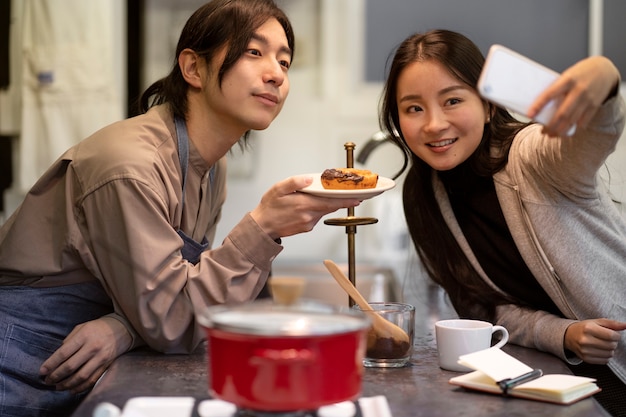 Japanese woman taking selfie with man and doughnut in a restaurant